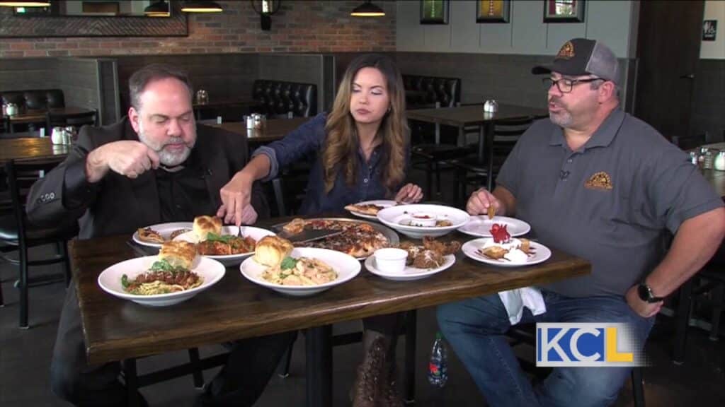 Two men with a woman eating at a restaurant