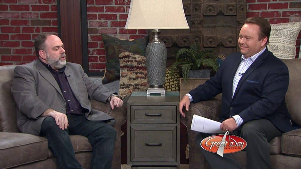 Two men with suits talking to each other sitting on the couch