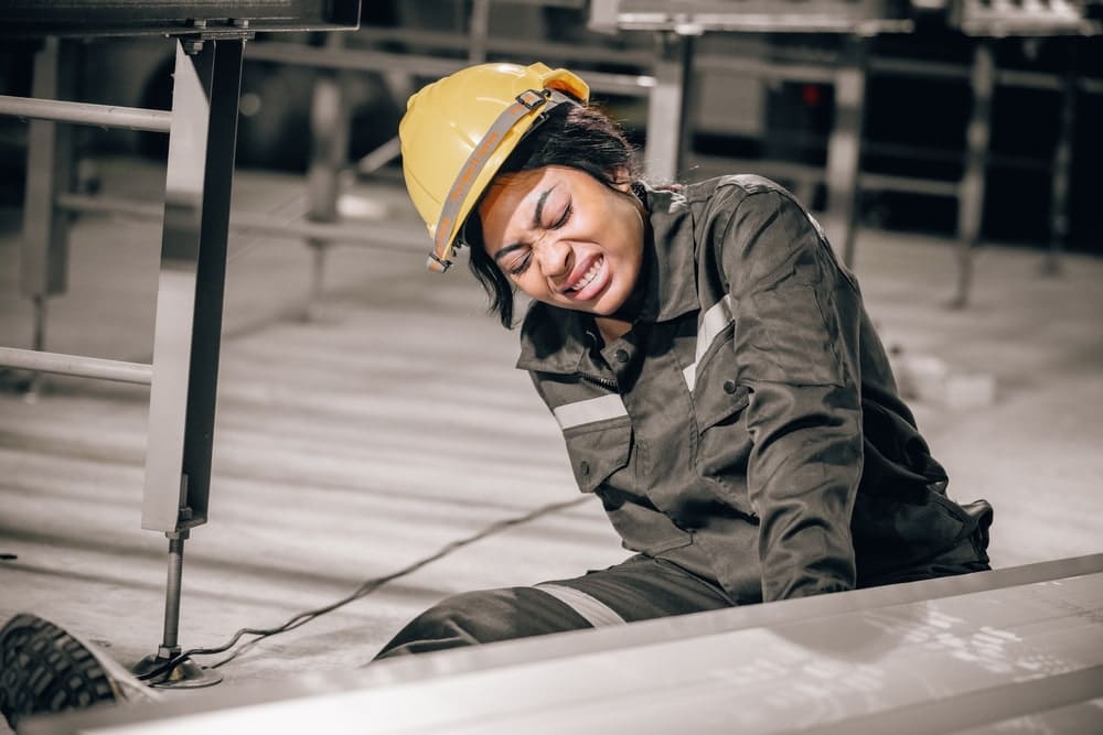 Female industrial worker in a hard hat grimacing in pain after an injury