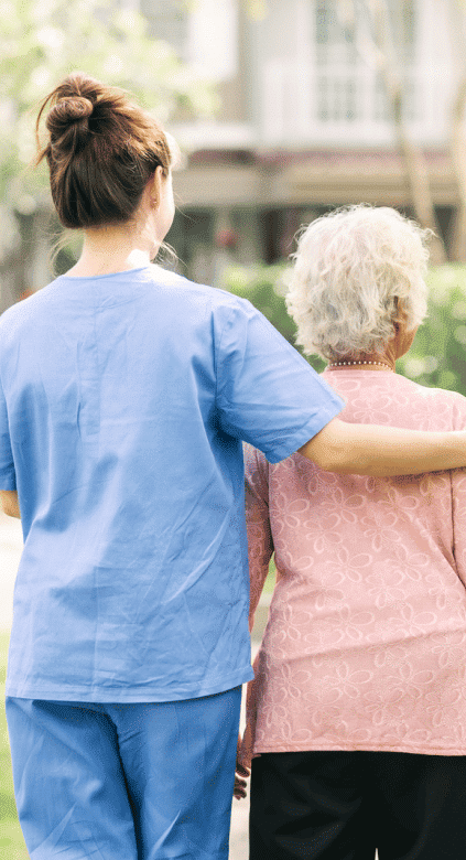 a female nurse supporting a senior woman walking
