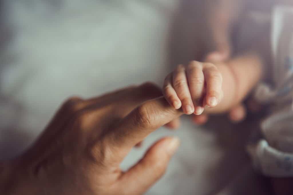 parent and infant holding each others hand - birth injury lawyer missouri