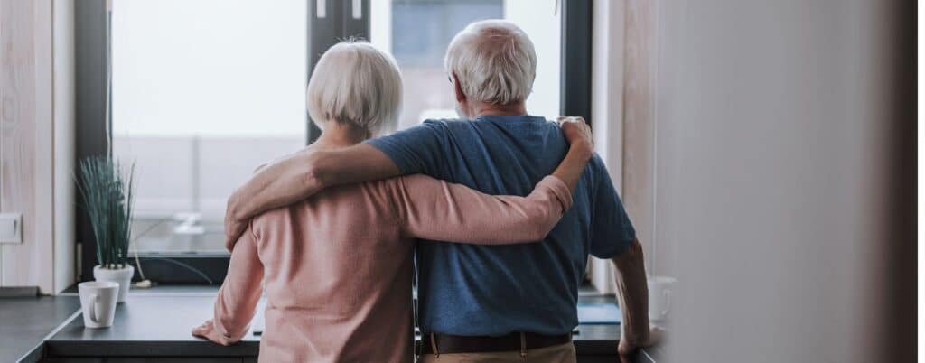 two elderly people embracing one another and looking out window