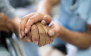 person holding hands with elder in nursing home