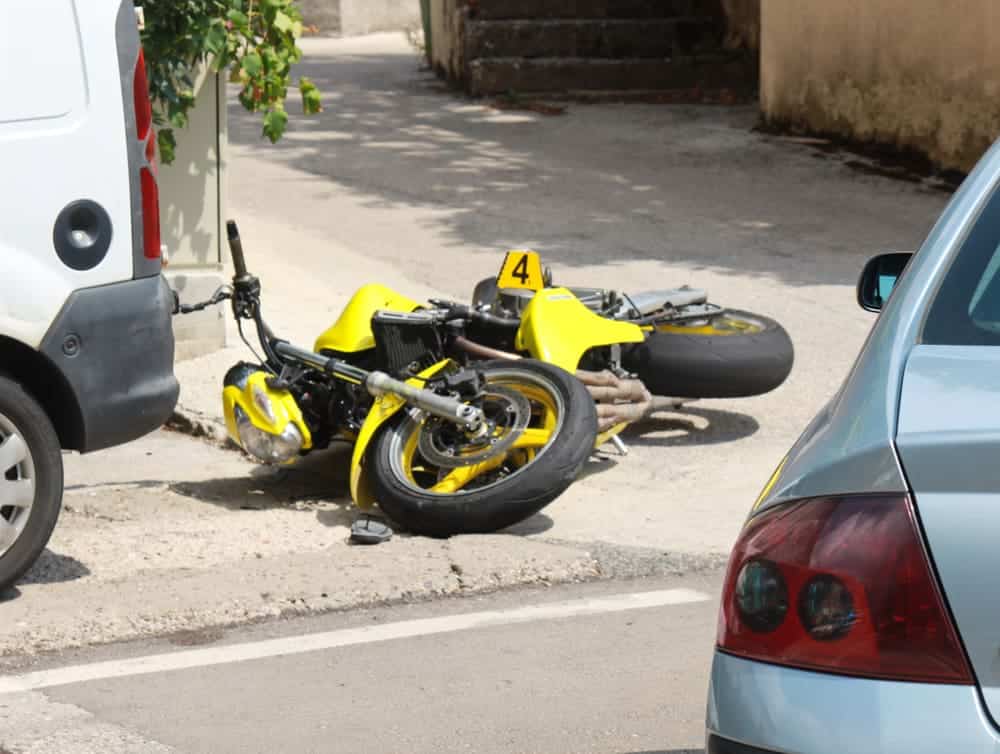 Yellow motorcycle down on the street after a collision with a car