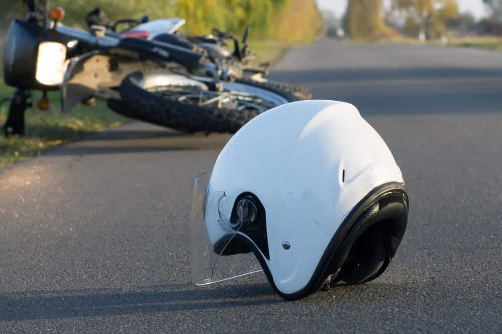 White motorcycle helmet on the road with a crashed bike in the background