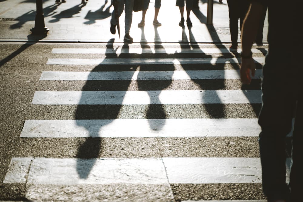Silhouettes of pedestrians crossing a crosswalk in backlit sunlight