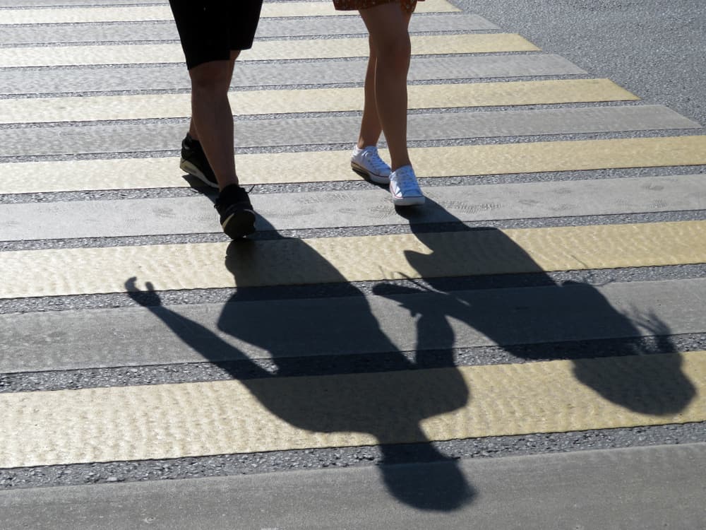 Two pedestrians walking across a crosswalk casting long shadows
