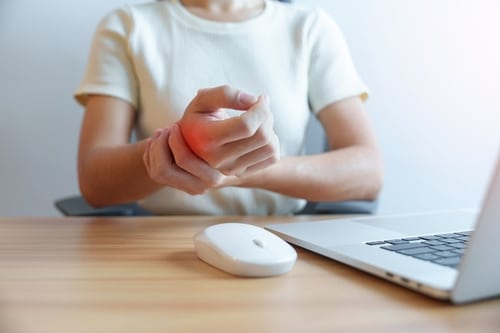 Person at a desk holding a wrist in pain from repetitive computer work