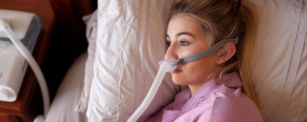 person in a hospital bed with CPAP machine on nightstand and mask on their face