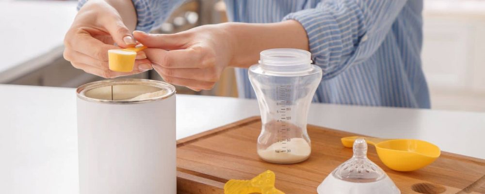 a person scooping baby formulas powder from a container into a baby bottle